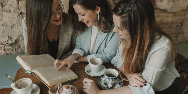 Three young women reading a book in a cafe