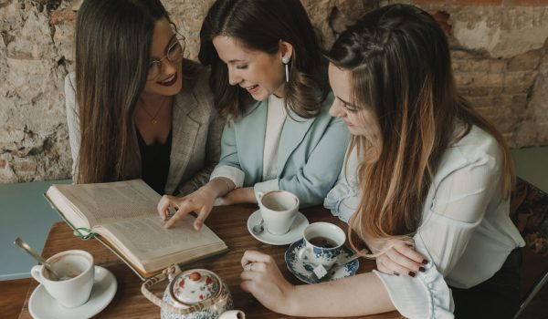 Three young women reading a book in a cafe